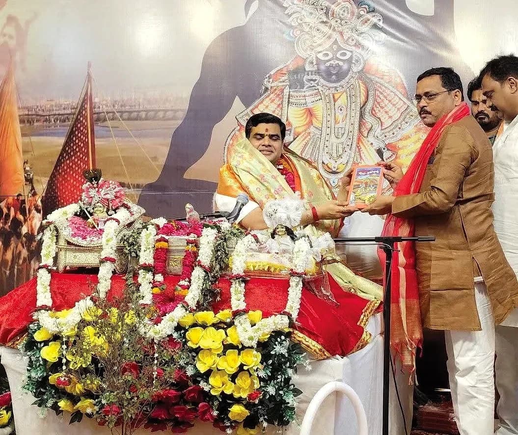 Vinod Kumar Upadhyay presenting a book to a seated guest at a religious and cultural programme